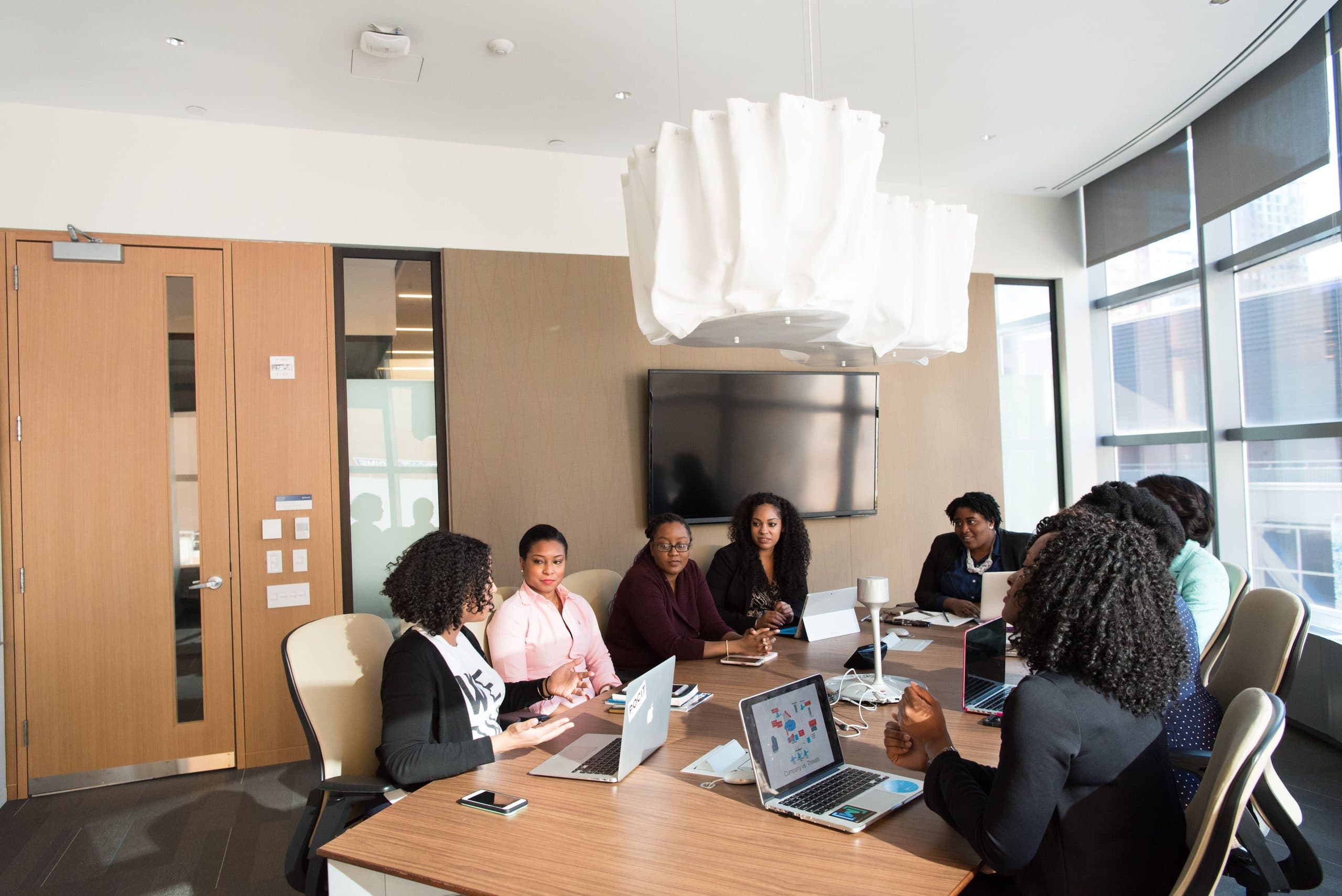 Professionals seated around a boardroom table with laptops open, in discussion.