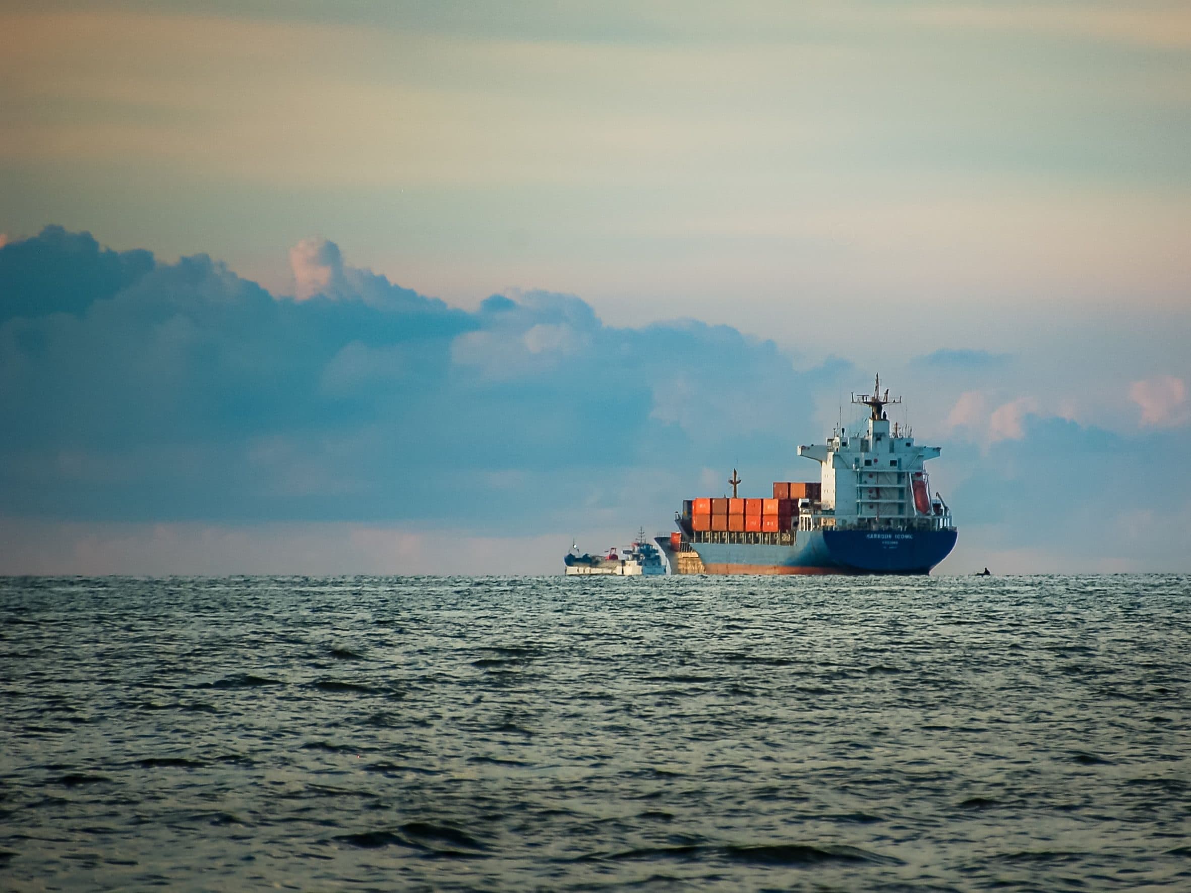 A container ship under way on open water beneath a wide band of cloud.