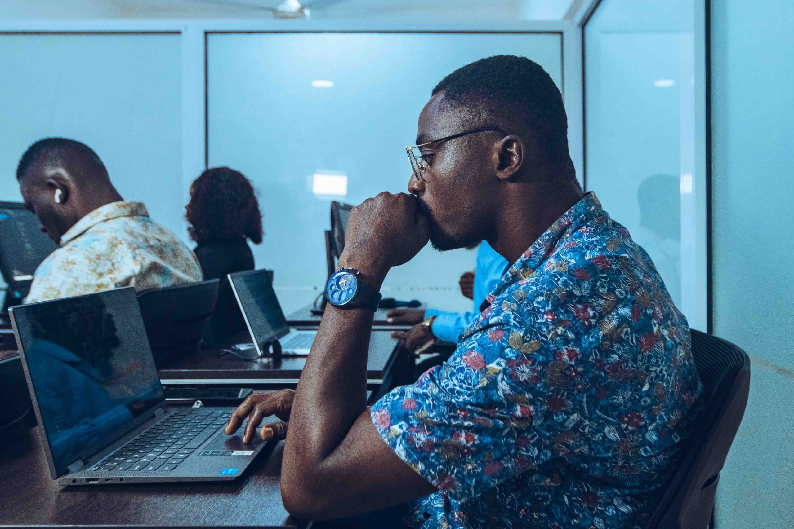 Adult learners working at laptops in an IT training room, one in the foreground concentrating on his screen.